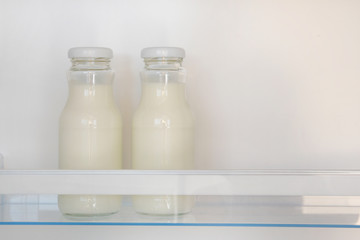 Dairy products in glass bottles on shelf of open empty fridge. White milk in  refrigerator. Horizontal view with copy space.