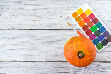 Fall Halloween crafts. One orange decorative pumpkin and bright paint with brush on white wooden...