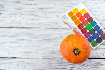 Fall Halloween crafts. One orange decorative pumpkin and bright paint with brush on white wooden background. Jack O Lantern Pumpkin on table ready for painting © irissca