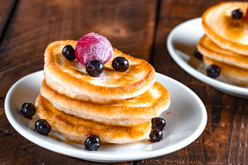 A plate of pancakes with fresh, frozen blueberries, cherries on a wooden background. Delicious, healthy breakfast.