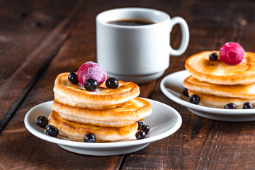 Homemade, delicious pancakes with fresh, frozen blueberries, cherries and a cup of coffee on a wooden background. Delicious, healthy breakfast. Fritters