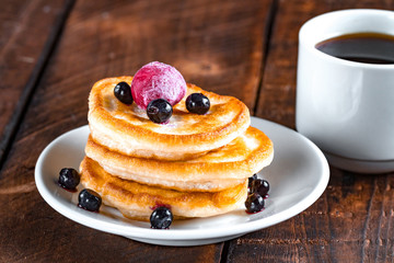 Homemade, delicious pancakes with fresh, frozen blueberries, cherries and a cup of coffee on a wooden background. Delicious, healthy breakfast. Fritters