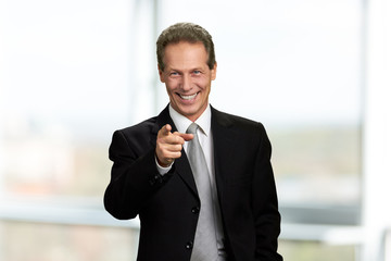 Happy businessman pointing with finger forward. Joyful mature man in business suit indicating with finger towards the camera.