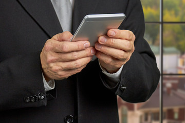 Close up businessman reading news on smartphone. Mature man in business suit looking at his smartphone close up, cropped image.