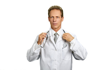 Doctor adjusting his stethoscope on white background. Male professional doctor in white coat looking seriously. Portrait of middle aged physician.