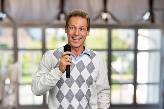 Happy smiling man holding microphone. Cheerful middle-aged man with microphone on abstract window background. Television presenter at tv programm.