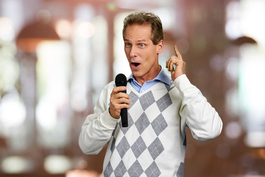 Elegant man talking into microphone. Cheerful man dressed in sweater talking into microphone on blurred background.