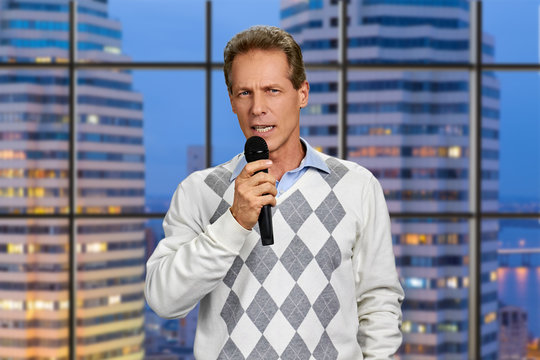 Man with microphone on skyscraper background. Confident middle-aged man talking into microphone on evening city background.