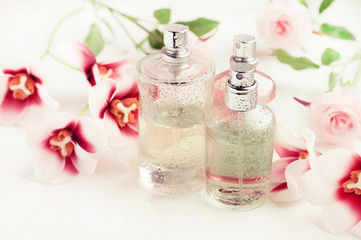 Light aroma perfume bottles wet with water drops surrounded by pink flowers on white bathroom...