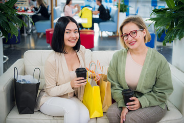 Fototapeta premium Portrait of smiling women with shopping bags and coffee to go looking at camera at the shopping mall
