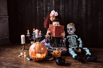 Group of cute multiracial kids in scary costumes reading horror stories in an old house, during...
