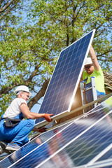 Two technicians standing on metal platform adjusting heavy solar photo voltaic panel on bright sunny day. Stand-alone solar panel system installation, efficiency and professionalism concept. © anatoliy_gleb