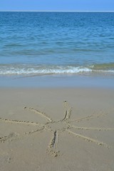 Sonne in den nassen Sand am Strand gemalt   mit Welle und blauem Himmel