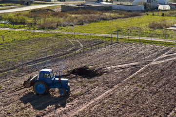 Fototapeta premium Fertilizing fields. Blue tractor fertilizing a field. Farmers spreading fertilizer with shovels.