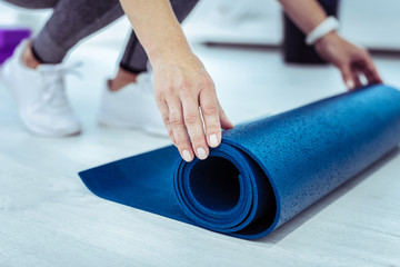 Preparation for training. Close up of tender female hands rolling out mat board while putting it on surface