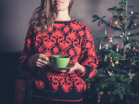 Young woman drinking tea by christmas tree