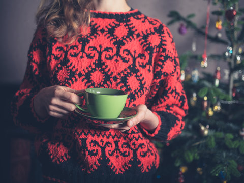 Young woman drinking tea by christmas tree