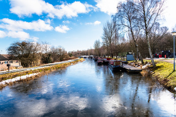 Frozen Canal with Colourful Canal Boats Moored to Jetties under Blue Sky With Clouds on a  Winter Day