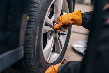 Picture of auto mechanics hands putting car tire on cr in workshop.