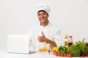 Chef man isolated over white wall background cooking make thumbs up gesture using laptop computer.