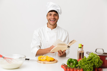 Young chef man isolated over white wall background cooking reading book.