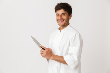 Young chef man standing isolated over white wall background holding knife.