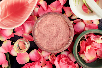 Pink cosmetic clay closeup with rose petals, ceramic bowls on black table, homemade skincare mask preparation