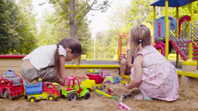 Crane shot. Three girls sitting in a sandbox and playing in the sand