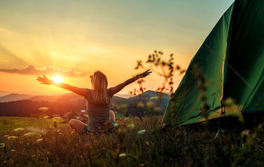 Happy woman with open arms stay near tent around mountains under sun