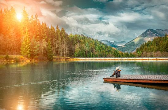 Happy young woman sitting on the wooden pier and drink coffee, lake, mountains background © Andrii IURLOV