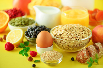 Delicious breakfast ingredients. Soft boiled egg, oat flakes, nuts, fruits, berries, milk, yogurt, orange, banana, peach on yellow background.