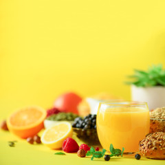 Orange juice, fresh berries, milk, yogurt, boiled egg, nuts, fruits, banana, peach for breakfast on yellow background. Copy space. Healthy food concept.