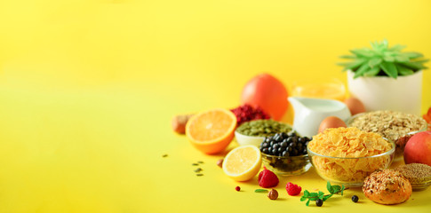 Vegetarian breakfast. Soft boiled egg, oat flakes, nuts, fruits, berries, milk, yogurt, orange, banana, peach on yellow background. Healthy food diet. Copy space. Banner