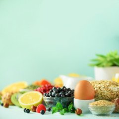 Healthy breakfast ingredients. Square crop. Oat and corn flakes, eggs, nuts, fruits, berries, toast, milk, yogurt, orange, banana, peach on blue background. Copy space