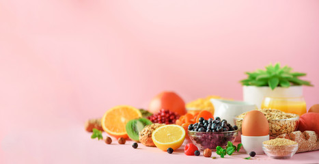 Healthy breakfast ingredients, food frame. Oat and corn flakes, eggs, nuts, fruits, berries, toast, milk, yogurt, orange, banana, peach on pink background. Top view, copy space. Flat lay © jchizhe