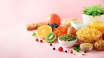 Vegetarian breakfast. Soft boiled egg, oat flakes, nuts, fruits, berries, milk, yogurt, orange, banana, peach on pink background. Healthy food diet. Copy space. Banner