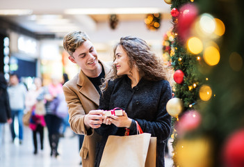 A young man giving a present to his girfriend in shopping center at Christmas.