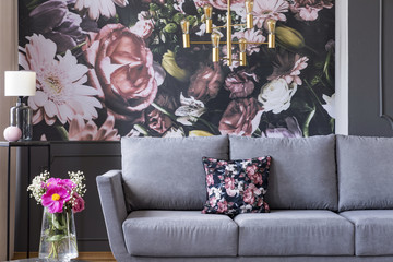 Real photo of a flower print behind a couch in a living room interior with fresh flowers in a vase