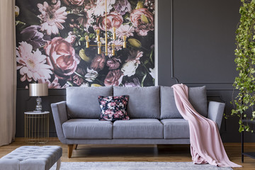 Real photo of a living room interior with a sofa, pillow, blanket and flowers on wallpaper - obrazy, fototapety, plakaty