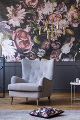 Elegant armchair, flower print on a wall and pillow on a floor in a daily room interior. Real photo
