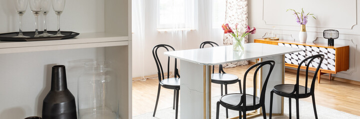 Black chairs placed by the marble table with fresh flowers in real photo of bright dining room...