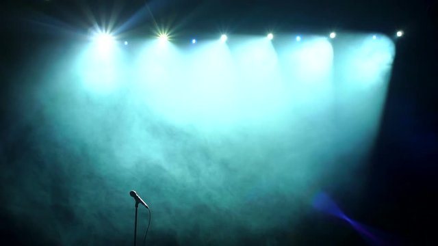 Close-up of microphone on stage in the dark against the background of professional concert lighting. Slow motion.