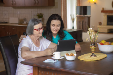 Caregiver with elderly woman using digital tablet at home