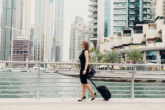 Young modern confident business woman pulling a suitcase in a Dubai Marine. Starting a new job in a big city.