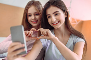 Expressing love. Beautiful females expressing positivity while taking photo on their gadget