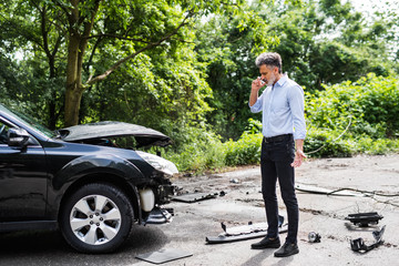 Mature man standing by the car, making a phone call after a car accident.