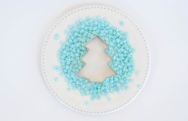 sugar decoration blue snowflakes and Christmas tree shaped dough cutter  on a plate on a white...