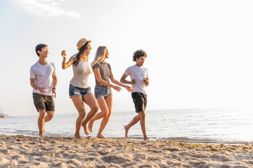 Group of friends having fun running down the beach at sunset.