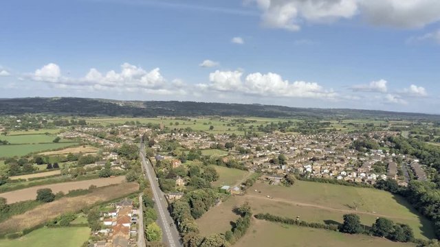 Aerial view, tilt down move. Traffic on roundabout, houses and fields in Tarvin on Cheshire countryside