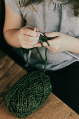 Young girl sitting at the wooden table and learning knitting with green yarn. Relaxing hobby, learning concentration.